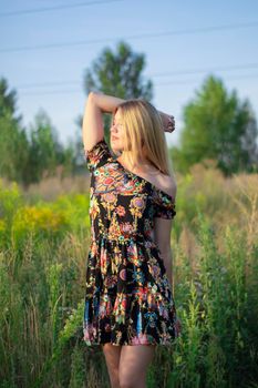 overlight bright portrait of a charming attractive blonde in flowery dress in the field.