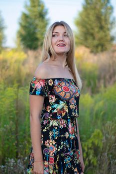 overlight bright portrait of a charming attractive blonde in flowery dress in the field.