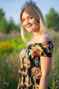 overlight bright portrait of a charming attractive blonde in flowery dress in the field.