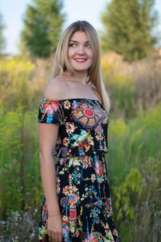 overlight bright portrait of a charming attractive blonde in flowery dress in the field.