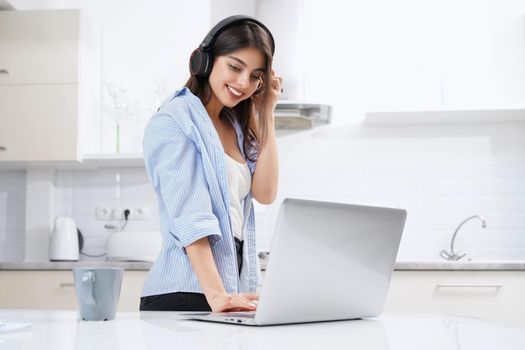 Smiling young woman smiling and working in laptop in kitchen. Concept of working at home.