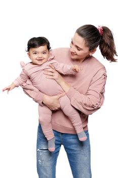 Portrait of cute mother holding daughter isolated on white studio background. Front view of young attractive woman hugging sweet adorable smiling baby girl while posing and looking at camera.