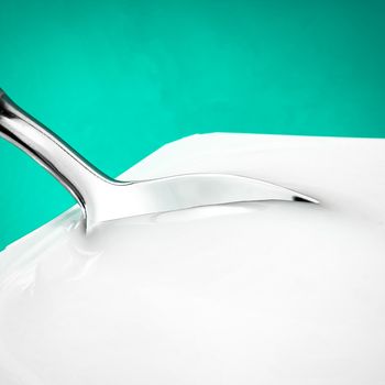 Yogurt cup and silver spoon on green background, white plastic container with yoghurt cream, fresh dairy product for healthy diet and nutrition balance.