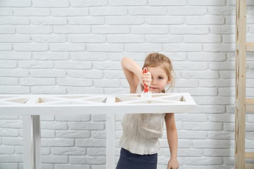 Little girl holding brush and painting wooden rack in white color. Concept of repair at home.
