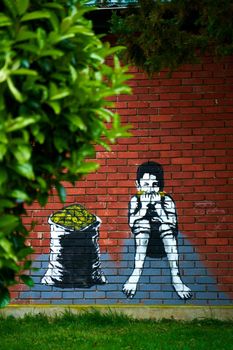 Graffiti drawing on a brick wall. A boy eats corn while sitting near a sack full of corn.