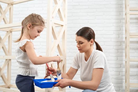 Young woman with child preparing dye for painting rack. Concept of improvement design at home.