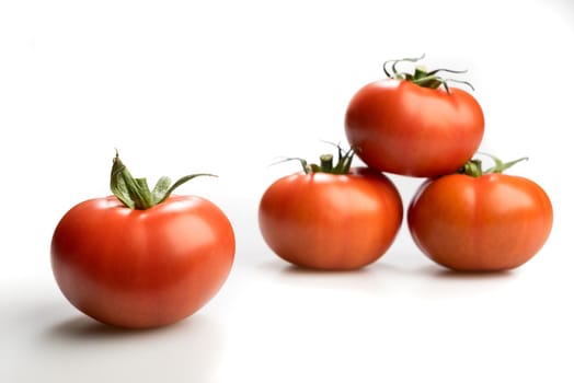 Four realistic looking fresh red tomatoes lying piled up isolated in a white background side view