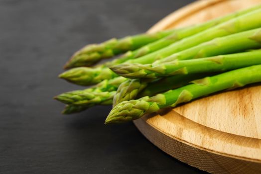 Asparagus spears close-up. A bunch of fresh raw green asparagus on a wooden cut board on a dark grey background.