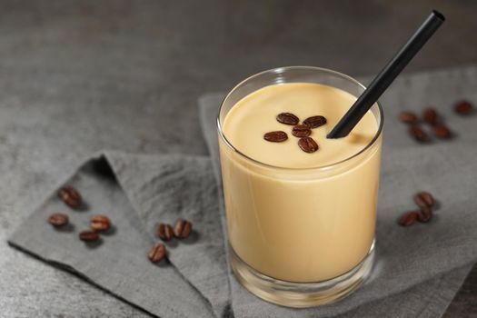 Cold coffee cream milkshake smoothie drink in a glass topped with coffee beans on a dark grey backdrop table with copy space.