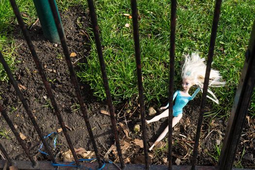 Lost doll lying behind a fence in the park