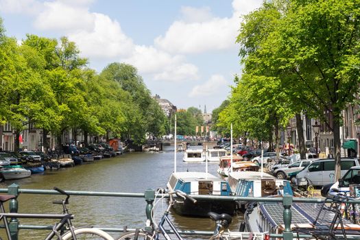 View from a bridge on the canals in Amsterdam with traditional houses, boats, bikes, trees and water in the Netherlands