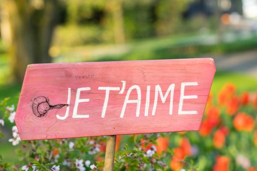 Pink sign in a field of flowers, tulips, saying  'I love you' in French "Je t'aime"