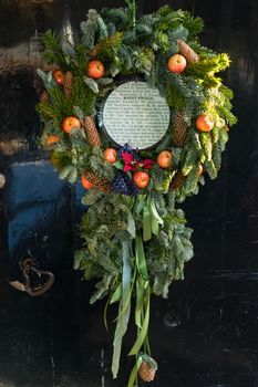 Wreath with branches of spur, pine, apples, cones and ribbons hanging on an old door