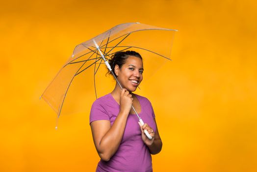 young attractive mixed race woman holding an umbrella wearing a purple shirt against a yellow background