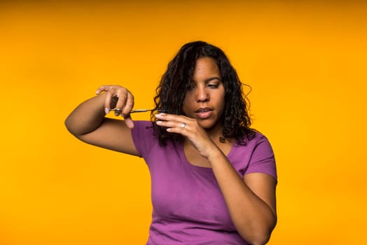 Young attractive mixed race woman cutting her hair in a yellow background