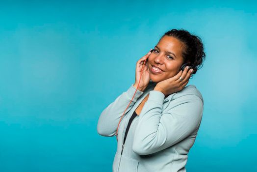 Young attractive mixed race woman enjoying music listening with headphones blue background