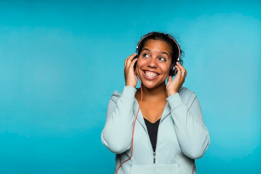 Young attractive mixed race woman enjoying music listening with headphones blue background