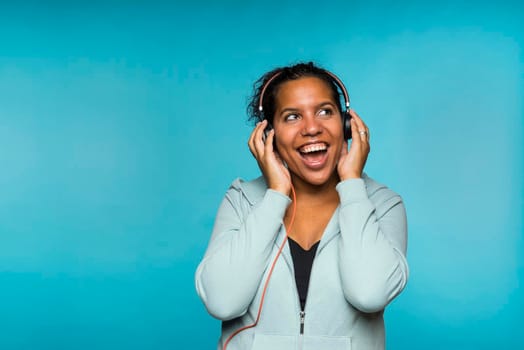 Young attractive mixed race woman enjoying music listening with headphones blue background