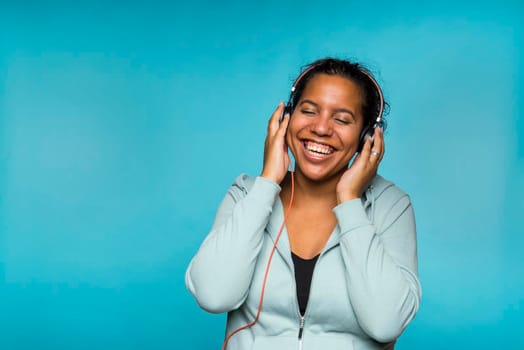 Young attractive mixed race woman enjoying music listening with headphones blue background