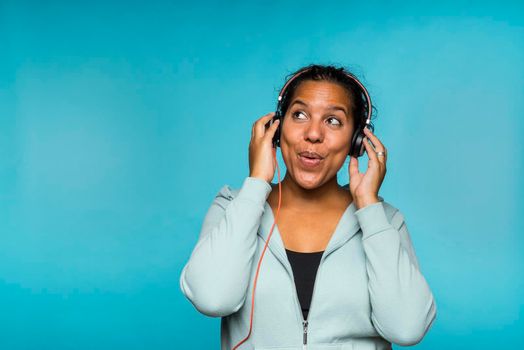 Young attractive mixed race woman enjoying music listening with headphones blue background