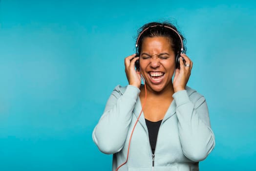 Young attractive mixed race woman enjoying music listening with headphones blue background