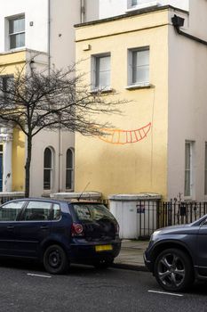 Yellow building with two windows and a smile drawn on the wall resembling a smiling face in Chelsea London England