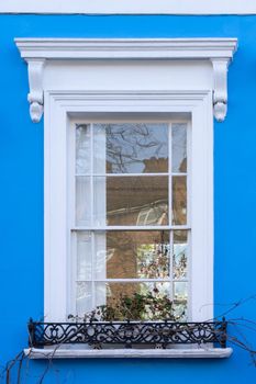 White window in a blue wall with a black metal bannister with plants on a window-ledge in London, England