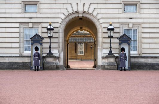 Entrance of Buckingham Palace - England - United Kingdom - with (unrecognizable) Welsh Guards in blue uniform standing guard and seethrough the gate to the inner court on a sunny day