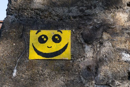 A yellow smiley is painted at a plate tagged to a stone decaying wall at the Duisburg Landschafts Park Germany