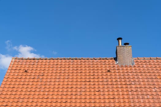 Roof with red roof tiles and chimney and a clear blue sky with some clouds on a sunny day