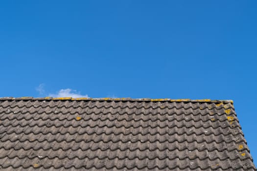 Roof with grey roof tiles and a clear blue sky with some clouds on a sunny day