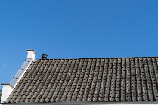 Roof with grey roof tiles and a clear blue sky with some clouds on a sunny day