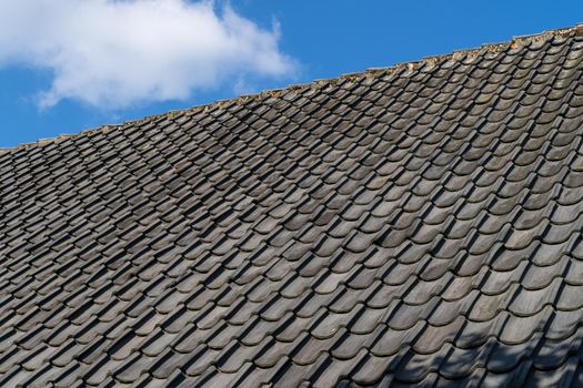 Roof with grey roof tiles and a clear blue sky with some clouds on a sunny day