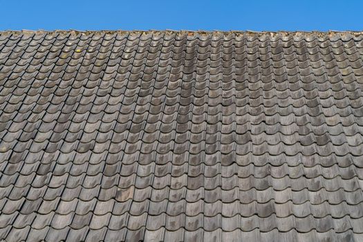 Roof with grey roof tiles and a clear blue sky with some clouds on a sunny day