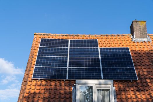 Roof with red roof tiles and solar panels for making renewable energy and a clear blue sky