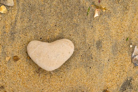 A close up of a yellow heartshaped pebble lying on a sandy beach in the South of the United Kingdom