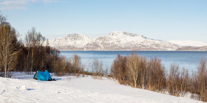 Blue tent on snowy field in the polar area with a view on a fjord and mountains covered in snow near Tromso Norway