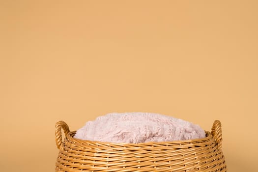 A close up of an empty basket with a pink cushion against a beige creme background