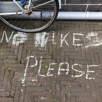 Pavement of small bricks with chalk letters reading ‘No bikes please’ and a parked bike showing disobedience