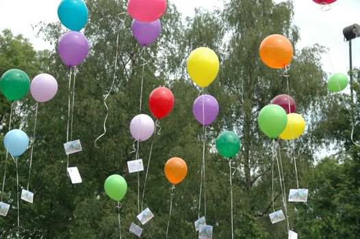 Large group of many colored balloons rising in the sky at a party with trees in the background