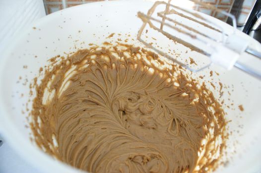 A brown cake batter in a white bowl whisked with a nice pattern and a kitchen mixer