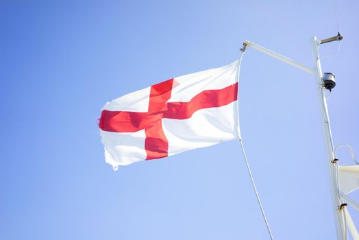 a English flag on a flagpole on a boat against a blue sky with soft clouds in the summer