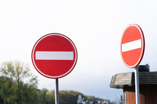 Two red circular traffic signs or roadsign with  white bar indicating no entry on a grey metal post against a cloudy sky in a forest area
