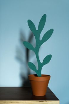 An artificial wooden plant shape in a terracotta pot on a wooden table on a blue background. The concept of office interior, home comfort, lifestyle. Mock-up with copy space for your text.