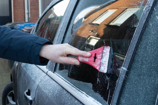 Cleaning the side car windows of snow with ice scraper before the trip. Man removes ice from car windows. A male hand.