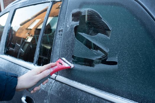 Cleaning the side car windows of snow with ice scraper before the trip. Man removes ice from car windows. A male hand.