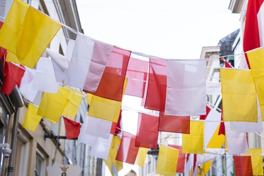 Many Dutch square flags on a ribbon, in red, white and yellow, of traditional festival named Carnaval, like Mardi Gras, in 's-Hertogenbosch, Oeteldonk with a blue sky