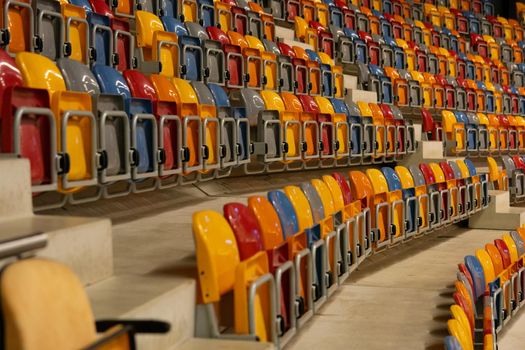 Rows of folded, green, blue, yellow, green and orange plastic seats in a very big, empty indoor stadium