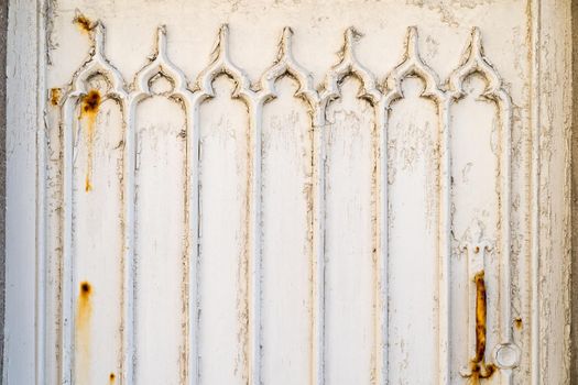 a Detail of a white wooden door with weathered and rusty paint and gothic window pattern relief