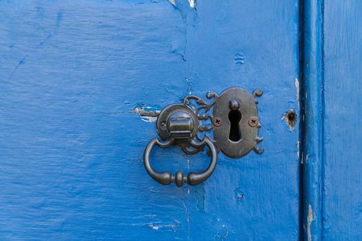 a Close up of an old doorknob knocker and a keyhole with a blue painted old weathered door with space fot text copy space